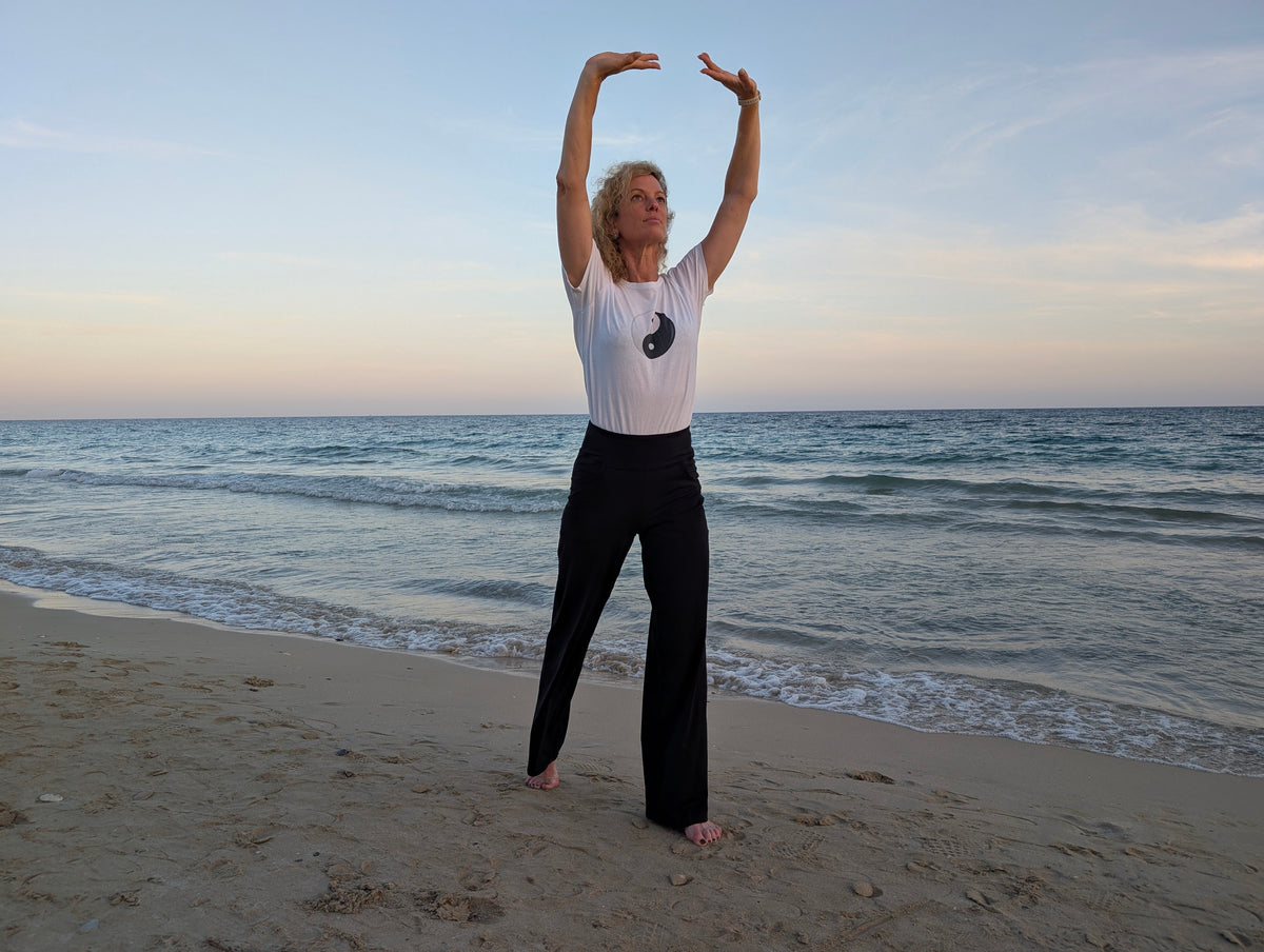 Kerstin Ottmann übt QiGong am Meer, die Arme über dem Kopf